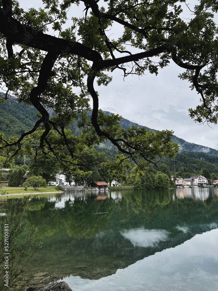 Picturesque view of lake with mountains and clouds reflections. Old small village. Scenic nature landscape. Summer vacation travel