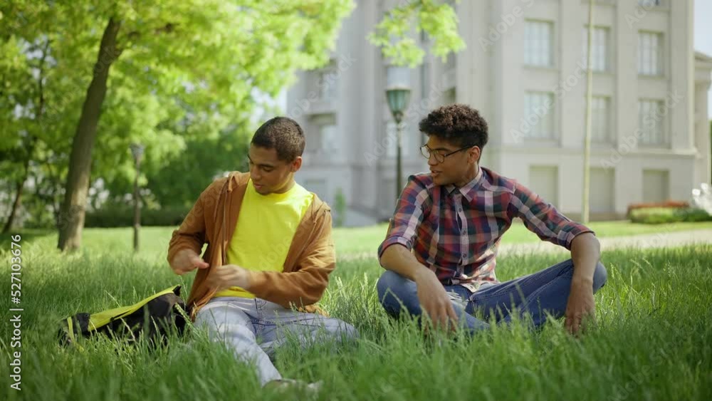 Two young men eating sandwiches after classes, hanging out together on campus Two young men eating sandwiches after classes, hanging out together on campus