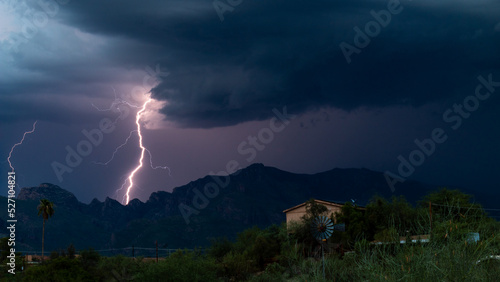 Lightning bolt and monsoon storm clouds over the Catalina Mountains in the Sonoran Desert north of Tucson, Arizona. Beautiful colorful moody sky, windmill, houses and natures furious beauty.