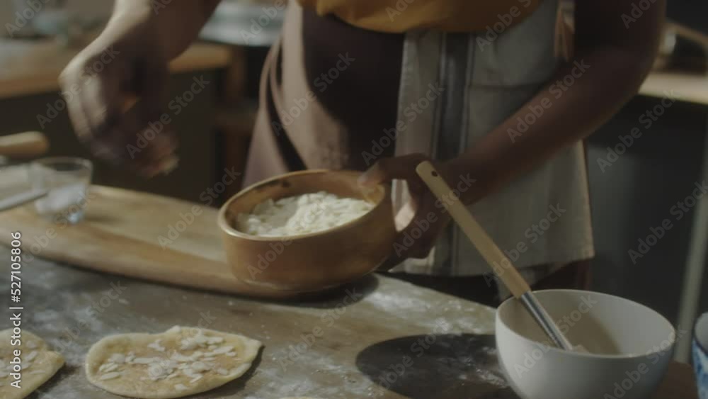 Cropped shot of African American woman adding almond flakes to dough while preparing pastry in kitchen at home