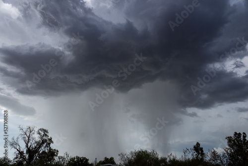 Monsoons in the Sonoran Desert with rain shafts or curtains coming down out of heavy dark gray clouds. Beautiful summer storm activity in the American Southwest. Pima County, Oro Valley, Arizona, USA.