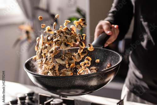 Close up of professional Chef cook hands roasts champignons with cream in wok pan for Mediterranean cuisine. Flying mushrooms in motion levitation.  photo