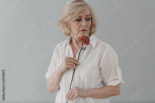 Foto Upset elderly woman in white dressed hold withered single one dry old rose flowe