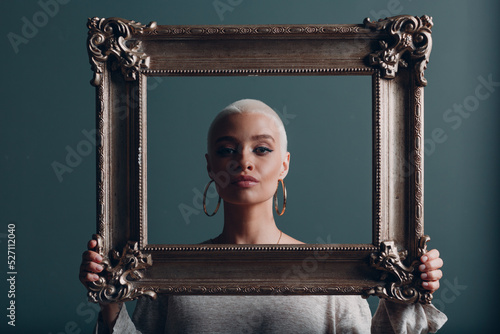 Quadro em tela Millenial young woman with short blonde hair holds gilded picture frame in hands