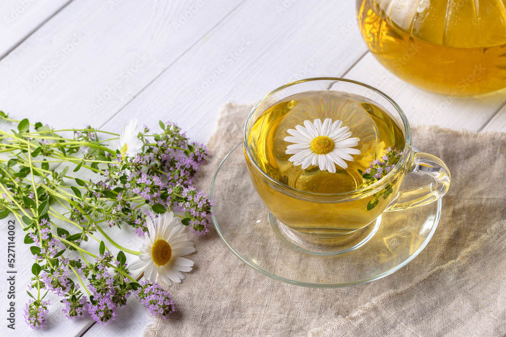 Herbal tea with chamomile and thyme in a transparent cup on a white wooden table Herbal tea with chamomile and thyme in a transparent cup on a white wooden table