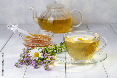 Herbal tea with chamomile and thyme in a transparent cup on a white wooden table