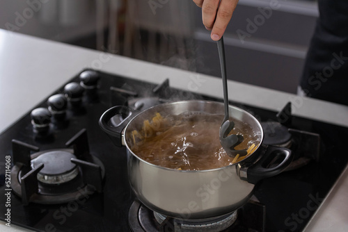 Professional chef cook making Italian Tagliatelle spaghetti pasta with at modern kitchen gas stove in pot. Boiling water. 