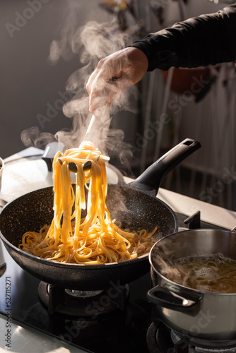 Professional chef cook making vegetarian Italian Tagliatelle pasta with mushrooms and cream at modern kitchen gas stove in wok pan.