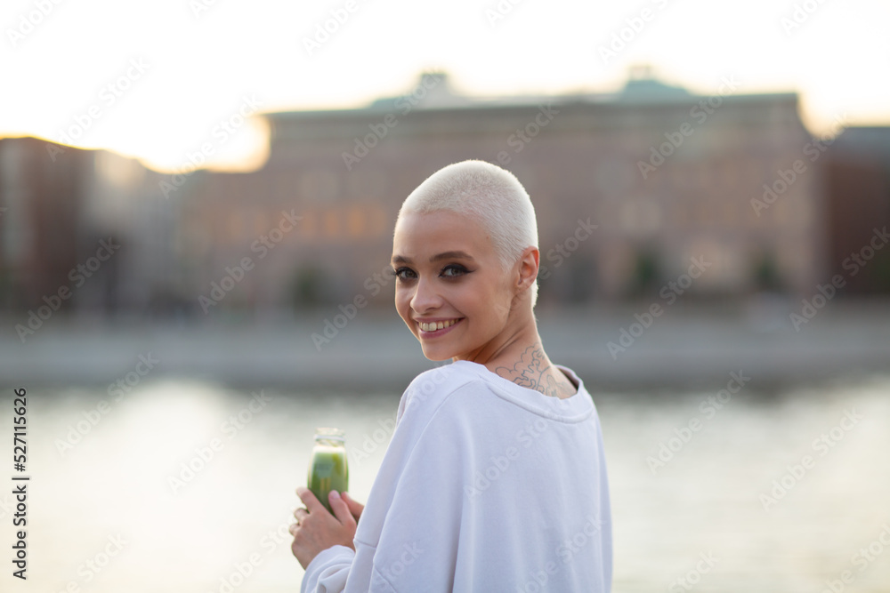 Portrait of young smiling millenial european short haired woman with green smoothie. Beautiful happy blonde girl outdoor. Portrait of young smiling millenial european short haired woman with green smoothie. Beautiful happy blonde girl outdoor.