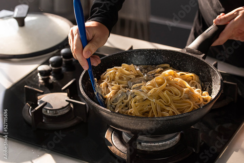 Professional chef cook making vegetarian Italian Tagliatelle pasta with mushrooms and cream at modern kitchen gas stove in wok pan.