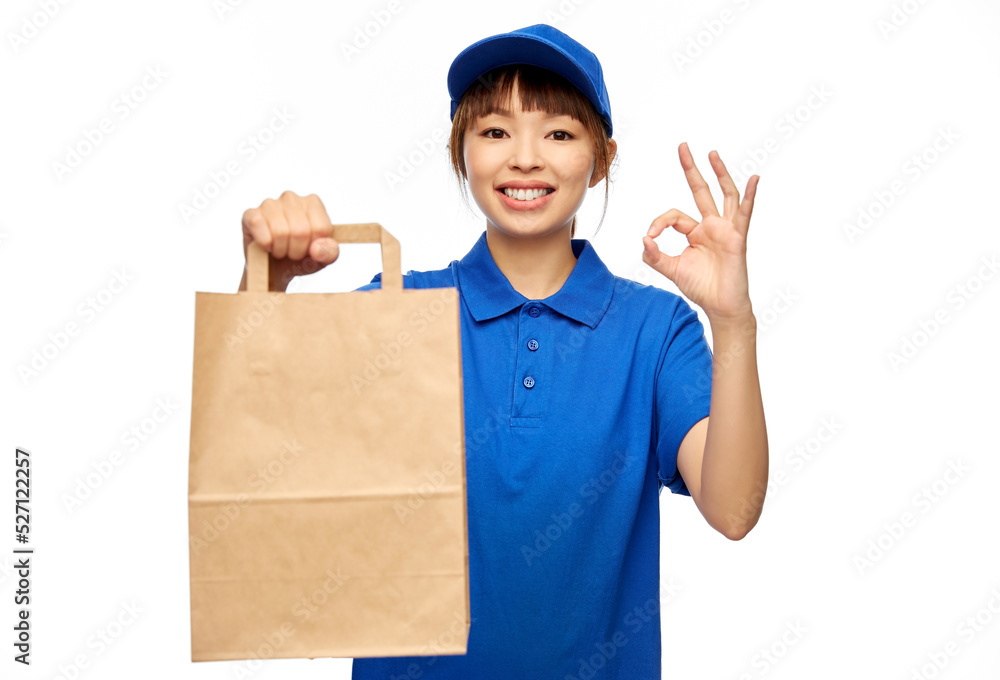 service and job concept - happy smiling delivery woman in blue uniform with takeaway food in paper bag showing ok gesture over white background service and job concept - happy smiling delivery woman in blue uniform with takeaway food in paper bag showing ok gesture over white background