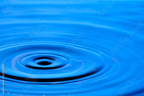 Splash drop of water with diverging water circles, on blue background.