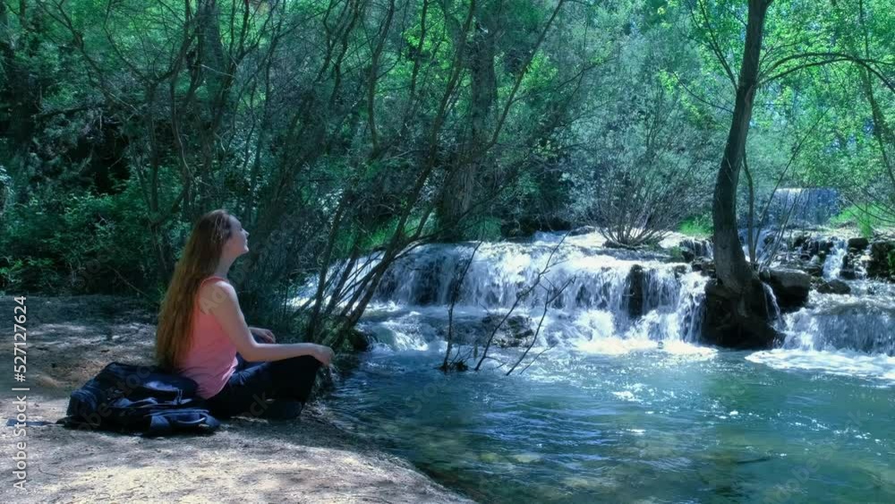 Woman is sitting and meditating in a nature with a waterfall. Woman is sitting and meditating in a nature with a waterfall.