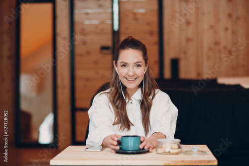 Smiling happy young woman sitting at table at home behind computer laptop and talking on video call. Girl female with cup of tea or coffee speaking online on webcam indoors photo