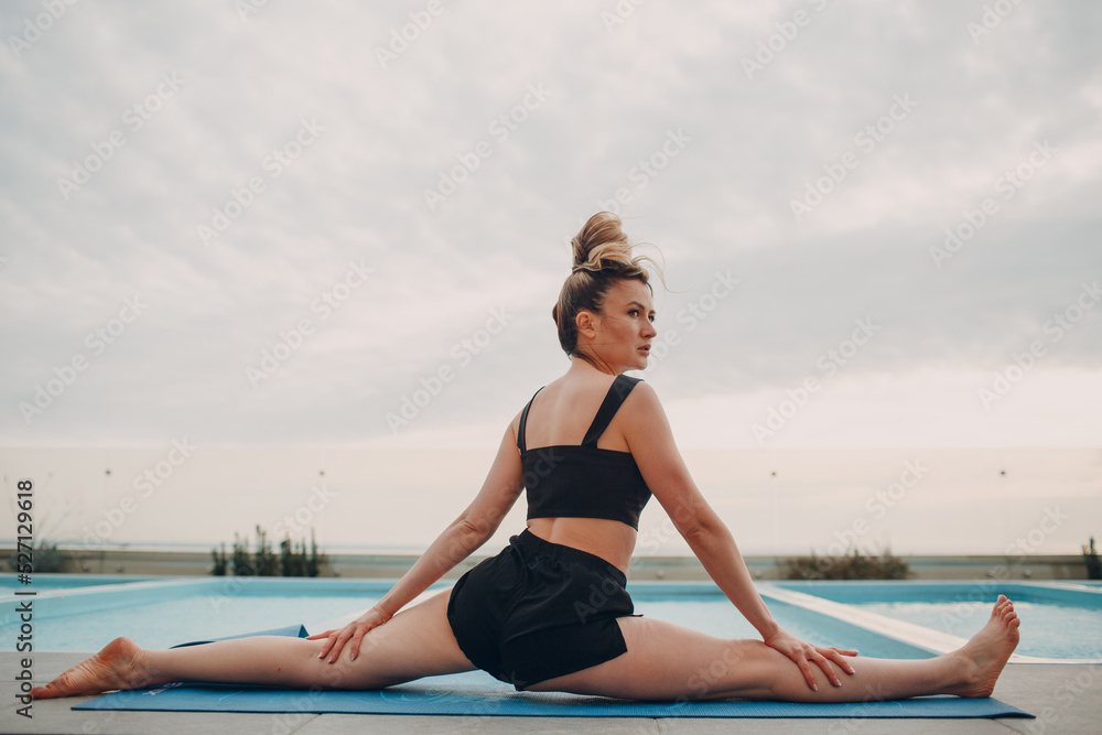 Caucasian woman practicing yoga at swimming pool and cloudy sky