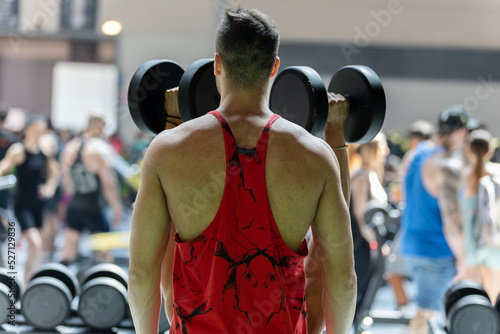 Boy in the Gym Ready to use Dumbbells in a Red Tank Top that highlights his Shoulders © GioRez