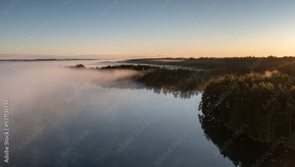 Aerial view over wilderness area with bog wetland and fog clad lake with the dawn colored sky background