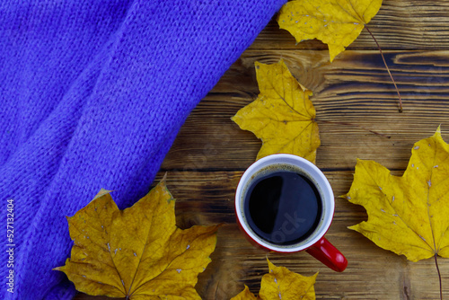 Cosy knitted blue sweater, cup of coffee and autumn maple leaves on wooden table. Top view. Autumn cozy concept
