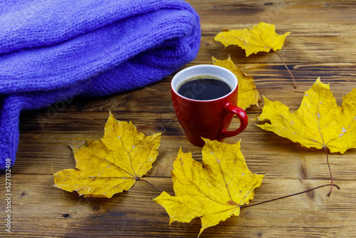 Cosy knitted blue sweater, cup of coffee and autumn maple leaves on wooden table. Autumn cozy concept