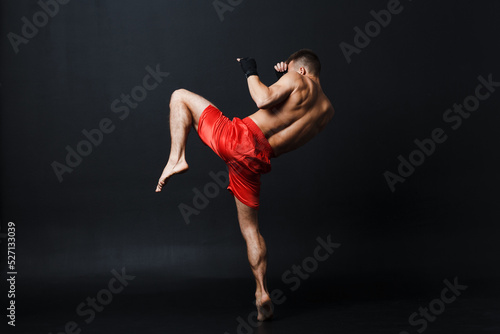 Sportsman muay thai man boxer stance ad knee kick at black background.