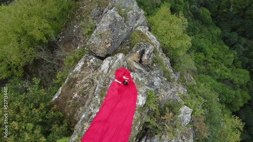 A girl in a red dress sits on the edge of a cliff, summer, mountains and forest, a seed from a drone