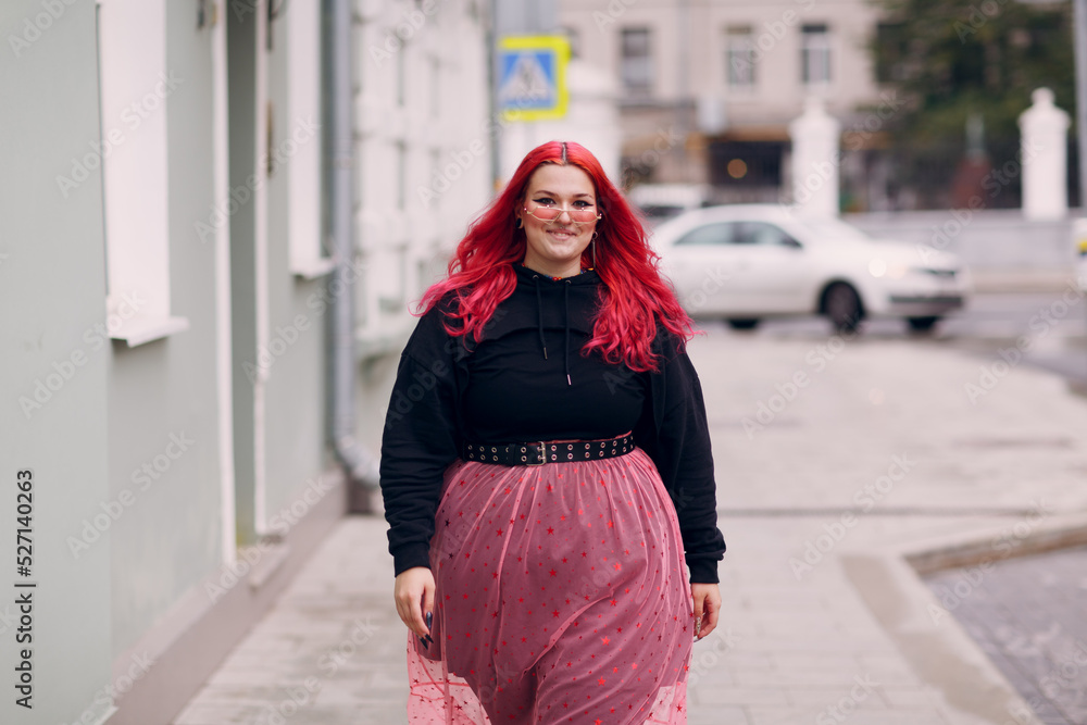 European plus size woman. Young red pink haired body positive girl walk at city street outdoors