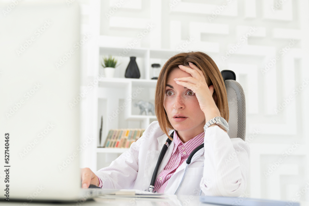 Close up portrait of tired female doctor sitting at the desktop and working on laptop in the office of modern clinic Close up portrait of tired female doctor sitting at the desktop and working on laptop in the office of modern clinic