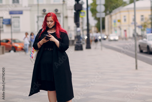 European plus size woman walking outdoor street city with mobile cellular phone. Young red pink haired body positive girl using cellphone smartphone © primipil