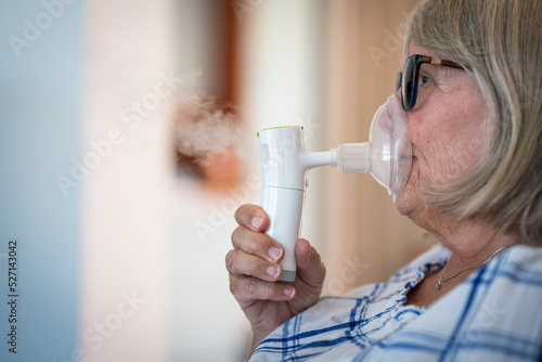 Senior lady breathing through oxygen inhaler at home. Medical and treatment concept.