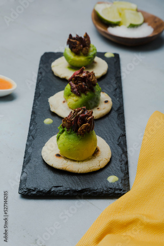 small corn tortillas with avocado and toasted grasshoppers accompanied by habanero chili sauce.