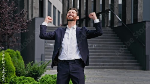 Excited happy businessman standing outdoors rejoicing in victory young male manager entrepreneur celebrating business success promotion professional achievement getting promoted making yes gesture photo