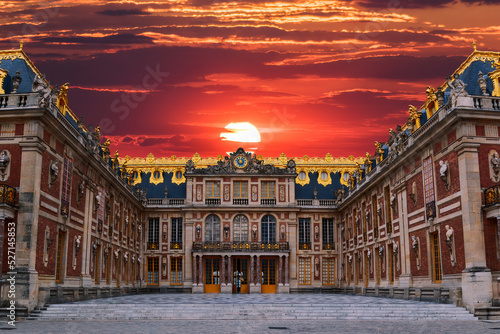 The main entrance to the Palace of Versailles just outside Paris, France is seen under a colourful red and orange sunset. photo