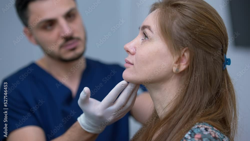 Side view face of beautiful Caucasian woman with blurred Middle Eastern plastic surgeon examining imperfections talking at background. Concentrated attractive lady consulting professional doctor Side view face of beautiful Caucasian woman with blurred Middle Eastern plastic surgeon examining imperfections talking at background. Concentrated attractive lady consulting professional doctor