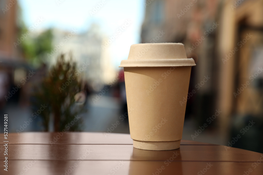 Cardboard takeaway coffee cup with lid on wooden table in city, space for text Cardboard takeaway coffee cup with lid on wooden table in city, space for text