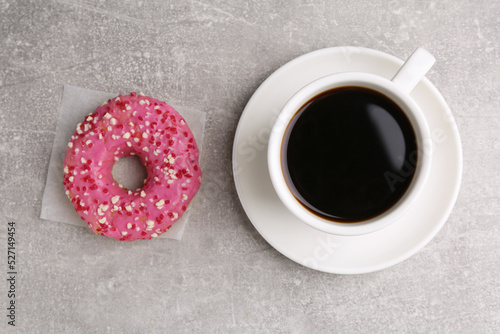 Tasty frosted donut and cup of coffee on light grey table, flat lay photo