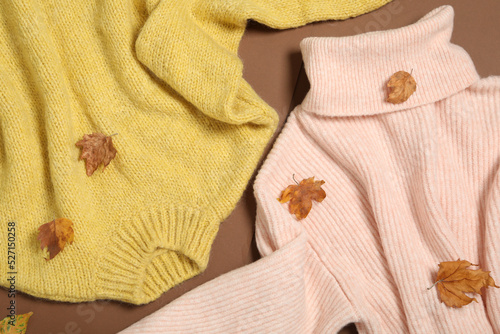 Warm sweaters and dry leaves on brown background, flat lay. Autumn season