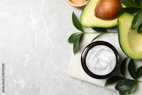 Jar of face cream and avocado on marble table, flat lay. Space for text