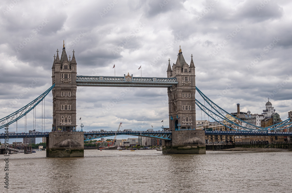 Fototapeta premium London, England, UK - July 6, 2022: Tower bridge seen from up brown water Thames on Western side under thick gray cloudscape.