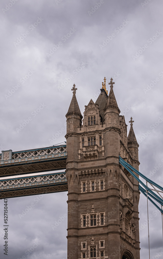 London, England, UK - July 6, 2022: Closeup of southern tower top section at Tower bridge seen from up brown water Thames on Western side under thick gray cloudscape.