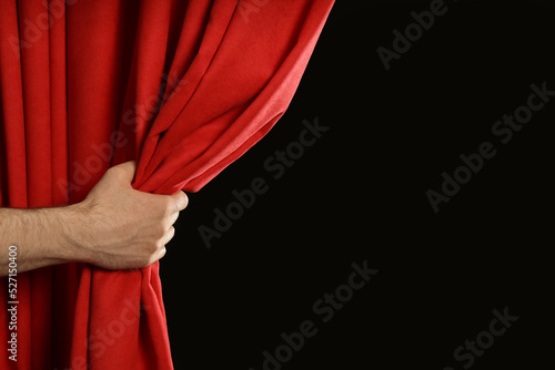 Man opening red front curtains on black background, closeup. Space for text