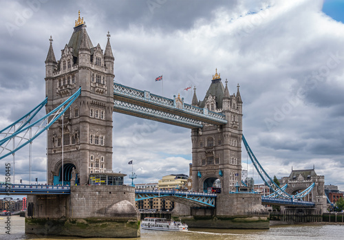 London, England, UK - July 6, 2022: Tower of London quay. White ferry sails in brown Thames water under Tower bridge. Thick coudscape above.  photo