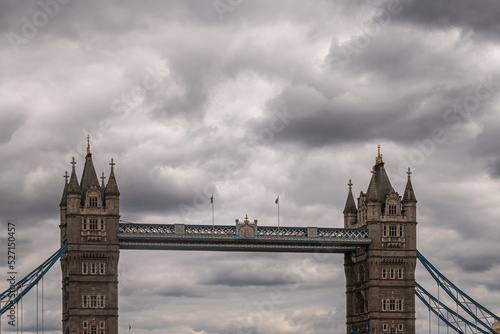 London, England, UK - July 6, 2022: Top half of Tower bridge seen from up brown water Thames on Western side under thick gray cloudscape.