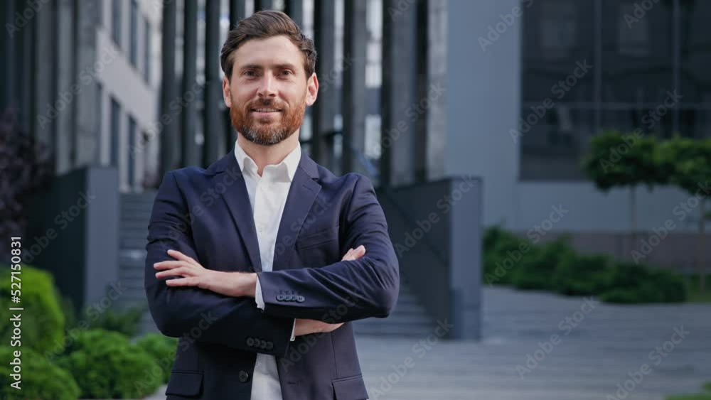 Successful confident businessman in stylish suit standing on background office building smiling looking at camera handsome caucasian male leader professional worker posing with crossed arms outdoors Successful confident businessman in stylish suit standing on background office building smiling looking at camera handsome caucasian male leader professional worker posing with crossed arms outdoors