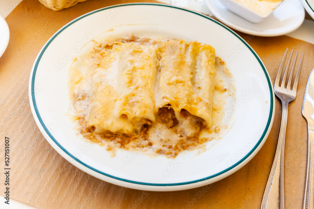 Appetizing Spanish style baked сannelloni filled with meat in creamy sauce with cheese served on plate..