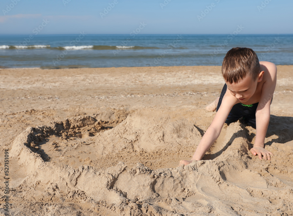 Little boy playing with sand near sea on sunny day Little boy playing with sand near sea on sunny day