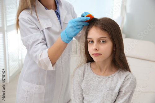 Doctor using nit comb on girl's hair in clinic. Anti lice treatment