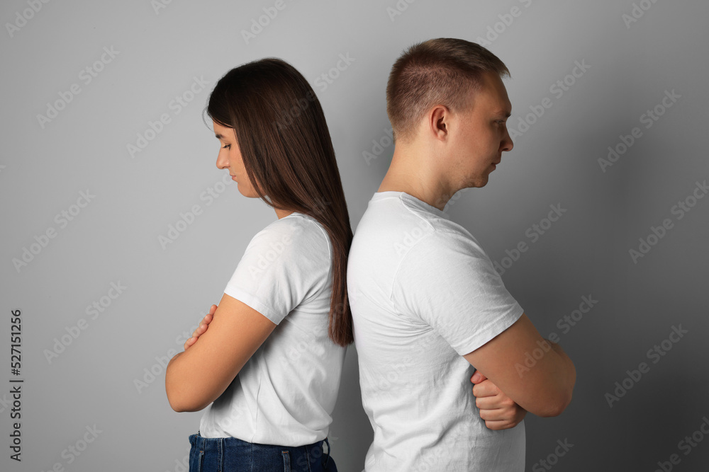 Unhappy young couple turning their backs on each other against light background Unhappy young couple turning their backs on each other against light background