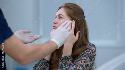 Caucasian woman touching face talking to unrecognizable plastic surgeon explaining facelift procedure. Portrait of confident beautiful female patient consulting professional Middle Eastern male doctor photo
