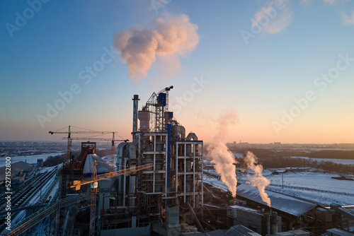Aerial view of cement factory with high concrete plant structure and tower cranes at industrial production area. Greenhouse gas smoke polluting atmosphere. Manufacture and global industry concept.