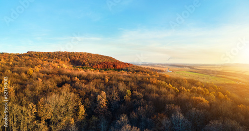 Aerial view of hills covered with dark mixed pine and lush forest with green and yellow trees canopies in autumn mountain woods at sunset. Beautiful autumnal evening landscape